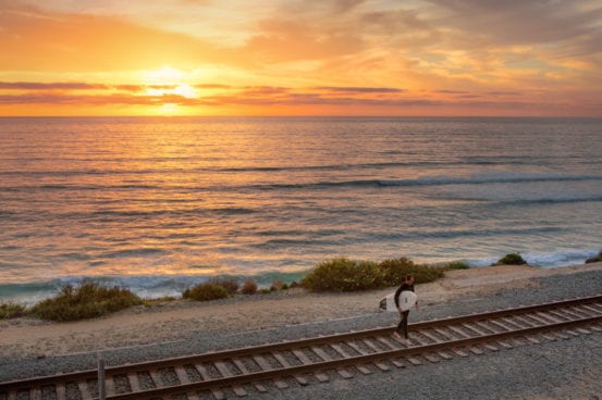 Surfer crosses the tracks at sunset in Del Mar